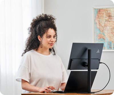 A woman is working from home with a desktop set up of a notebook and ZenScreen MB17AHG install on a tripod stand for a better comfortable viewing angle.