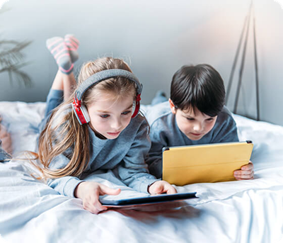 Zwei Kinder liegen auf einem Bett und benutzen ihre Tablets.